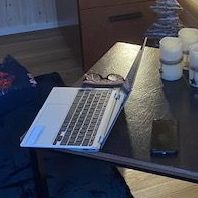 A laptop, glasses, and a phone on a wooden table with decorative candles.
