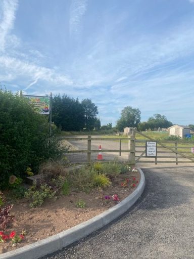 Entrance to a gravel path surrounded by greenery and flowerbeds under a clear blue sky.
