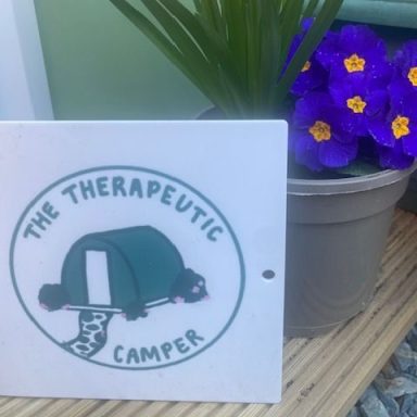 Logo of "The Therapeutic Camper" featuring a tent and decorative plants.