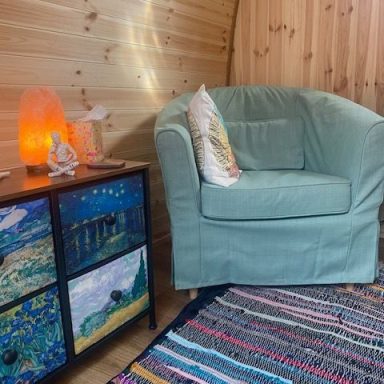 Cosy interior with two chairs, a heater, and a colourful rug in a wooden cabin.