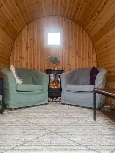 Cosy interior with two armchairs, a small table, and a wood stove against a wooden wall.